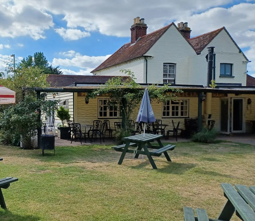 The beer garden at the Yew Tree Inn: a lawn with green picnic benches and parasols, and a covered terrace with cast iron tables along the back of the pub