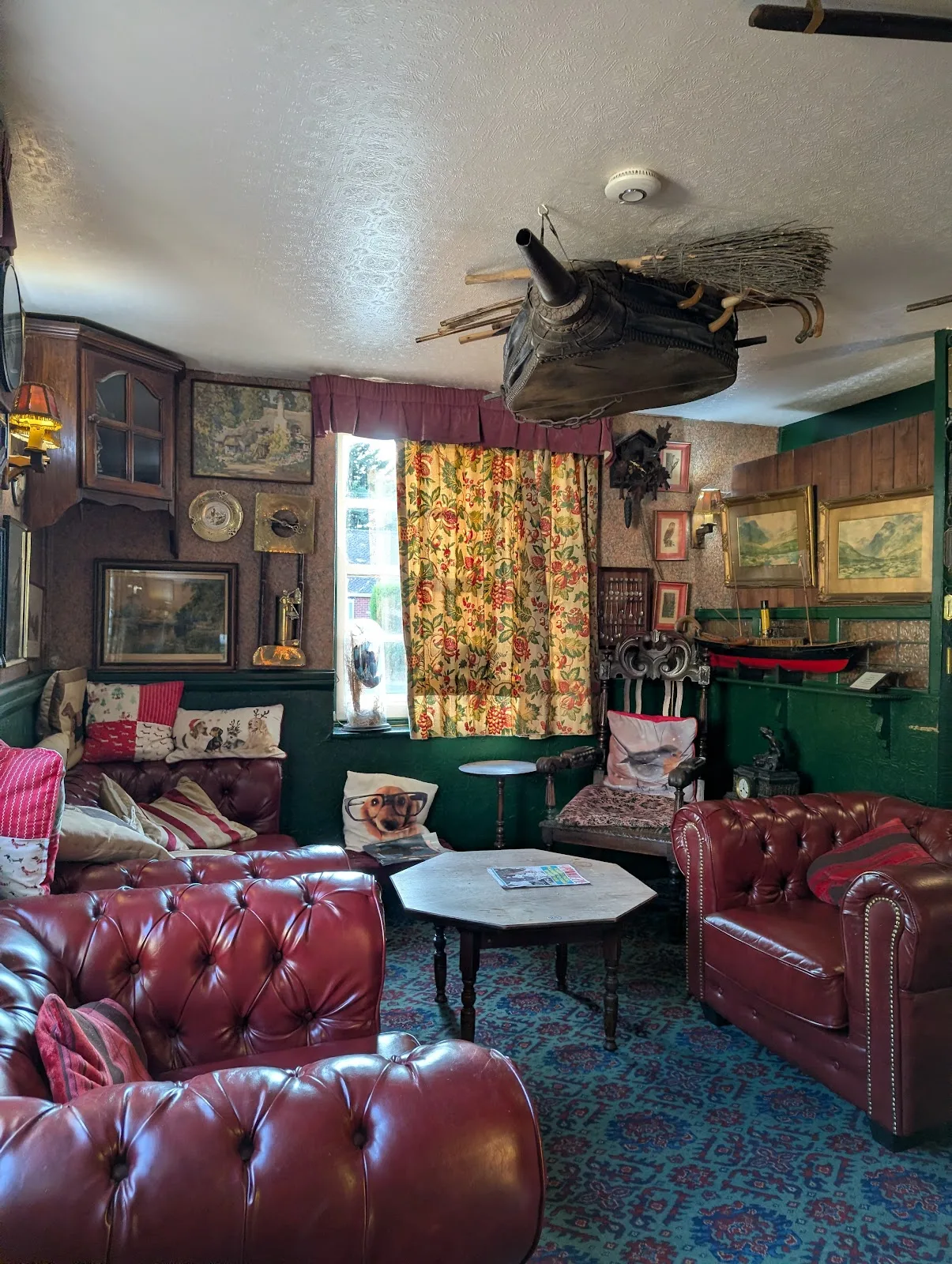 The lounge at the Yew Tree Inn with red leather chesterfields, green panelling and a leather fire bucket hung from the ceiling