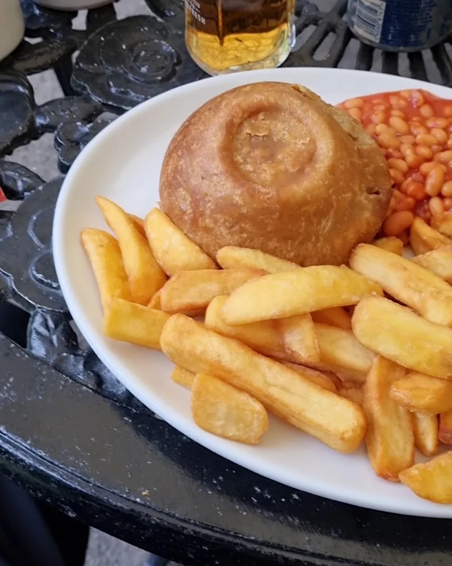 A suet pudding with chunky chips and baked beans on a cast iron table at the Yew Tree Inn, with a pint of lager